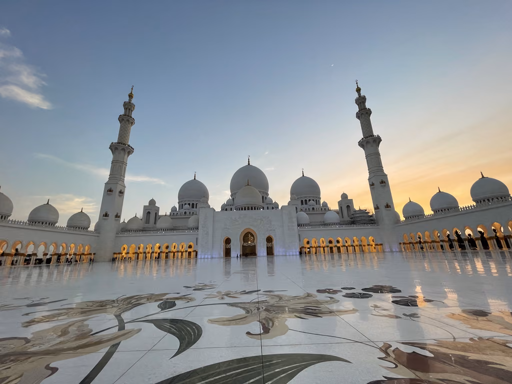 Sheikh Zayed Grand Mosque in Abu Dhabi at sunset, showcasing the white marble courtyard with intricate floral mosaics.
