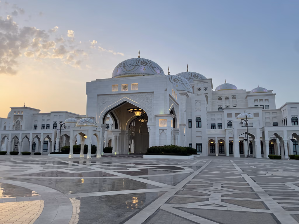 Grand white exterior of the Qasr Al Watan palace in Abu Dhabi with intricate domes and geometric courtyard tiling under a sunset sky.