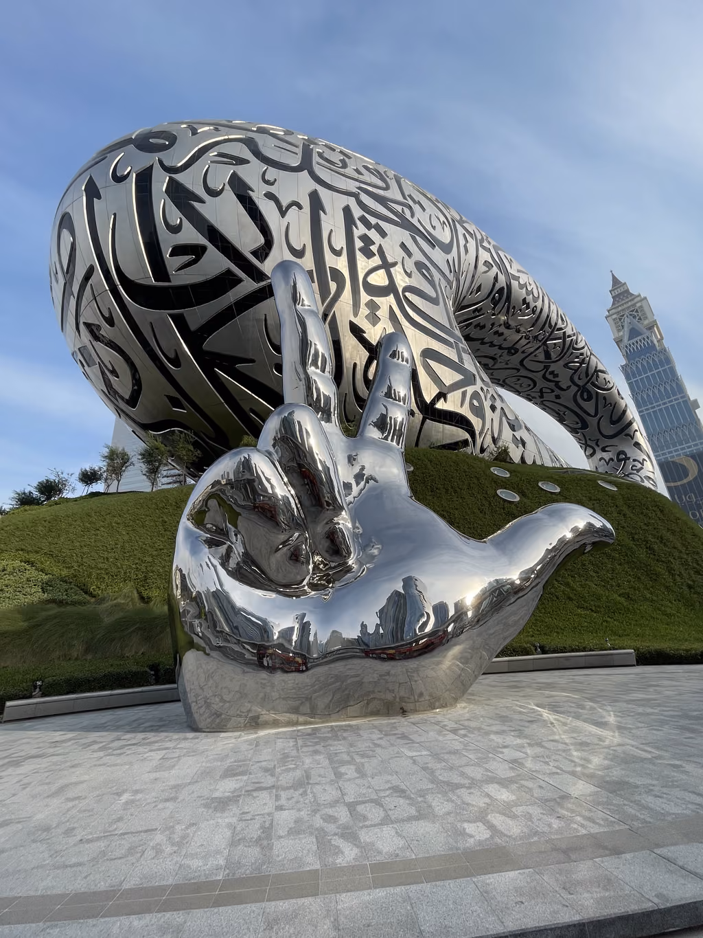 The iconic Museum of the Future in Dubai stands tall behind a striking mirrored hand sculpture.