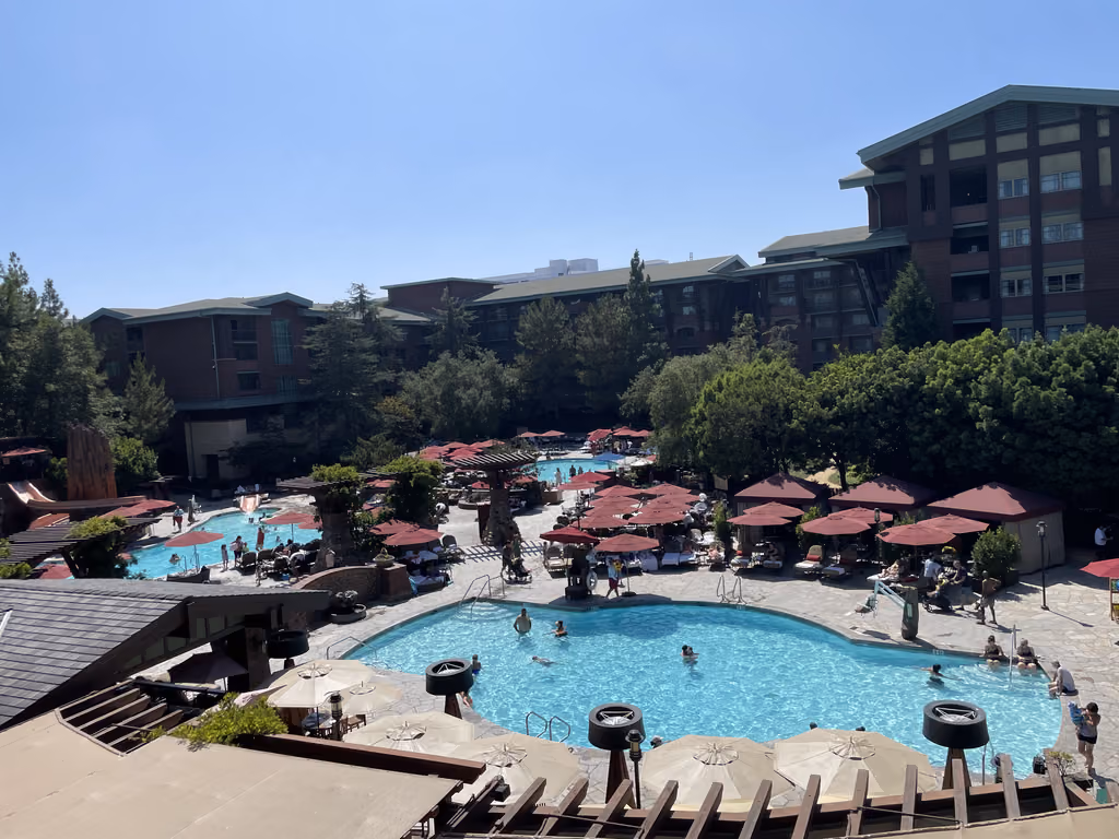 A high-angle view of the multiple swimming pools and red patio umbrellas at Disney's Grand Californian Hotel in Anaheim.
