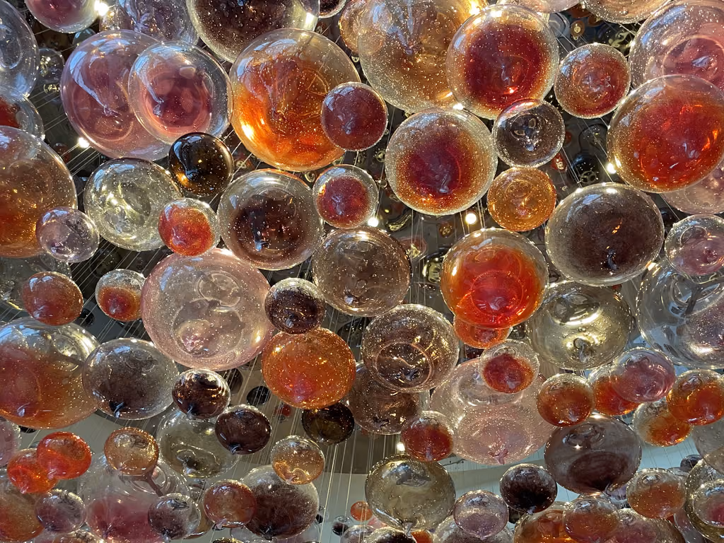 A close-up view of the intricate, multicolored glass orb sculpture hanging in the lobby of the Andaz Capital Gate hotel.