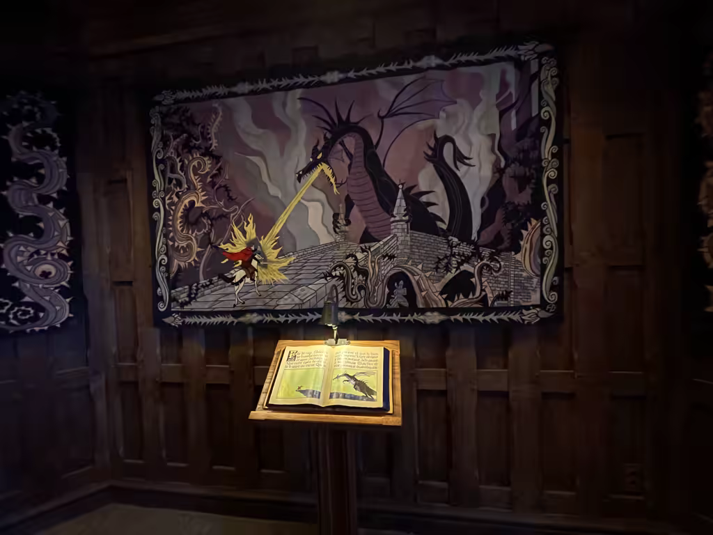 An ornate tapestry depicting a knight fighting a dragon hangs above an open storybook in the Sleeping Beauty Castle at Disneyland Paris.