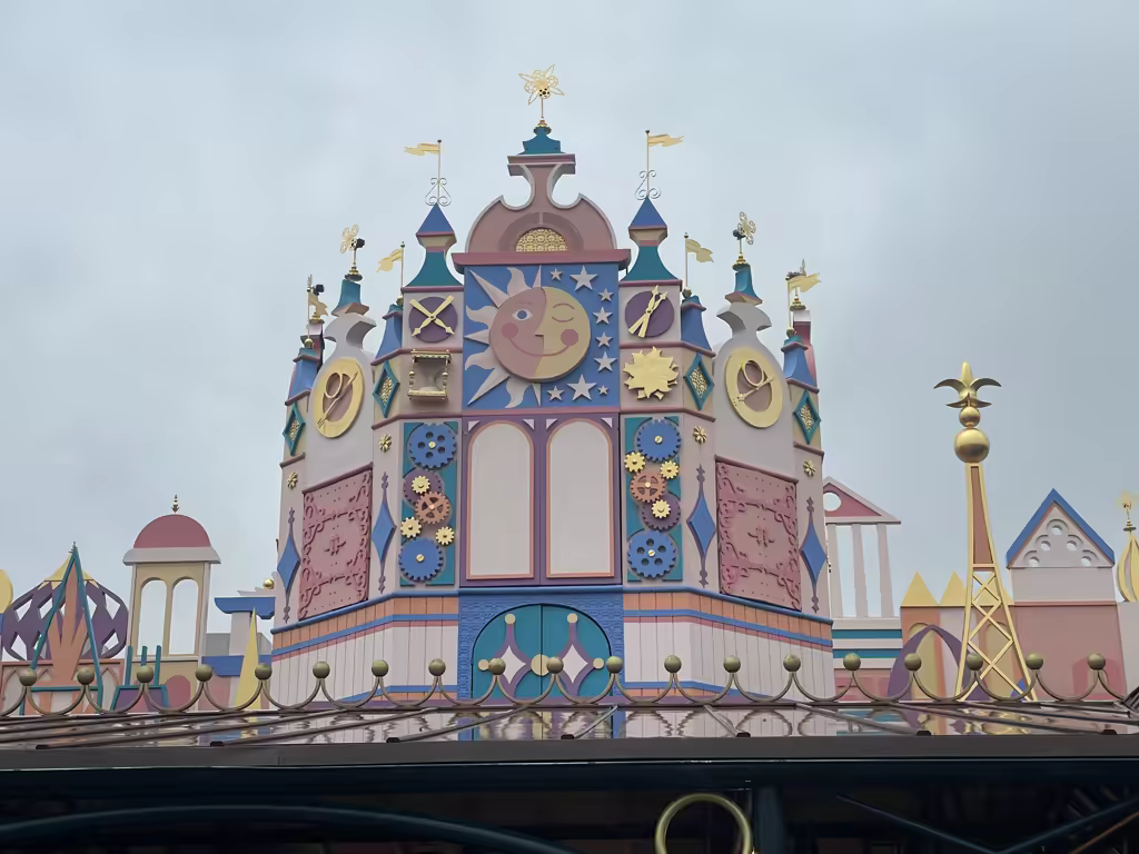 The colorful, clock-themed exterior facade of the 'it's a small world' attraction at Disneyland Paris under a cloudy sky.
