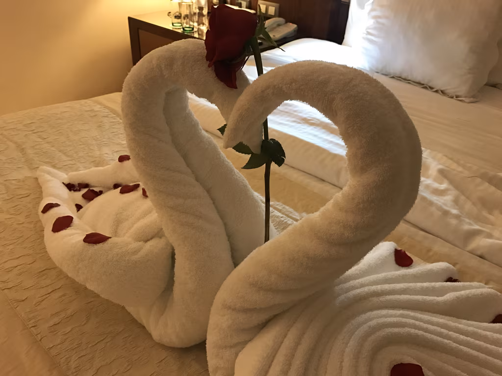 Two white towel swans shaped into a heart with a single red rose on a hotel bed at Excellence Playa Mujeres.