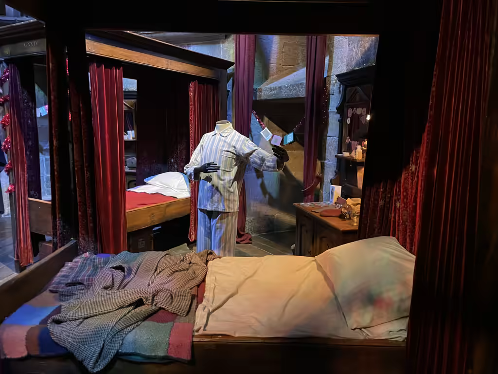 Harry Potter studio tour dorm room display featuring pajamas on a mannequin and wood-framed beds.