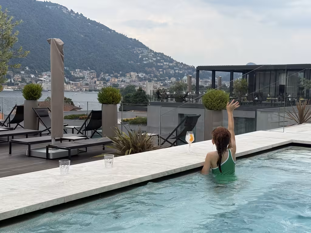 A child in a green swimsuit in the rooftop infinity pool at the Hilton Lake Como with views of the lake and mountains.