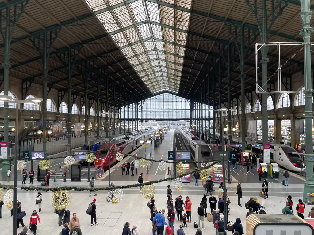 Wide angle view of the interior architecture of the historic Gare du Nord train station in Paris with high glass ceilings and trains at the platforms.