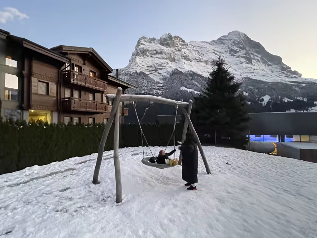 A child on a disc swing in the snow with the Eiger mountain peak in the background, Switzerland.