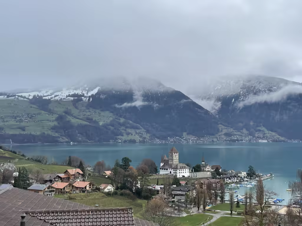 The iconic Spiez Castle stands prominently against a backdrop of snow-dusted peaks over Lake Thun.