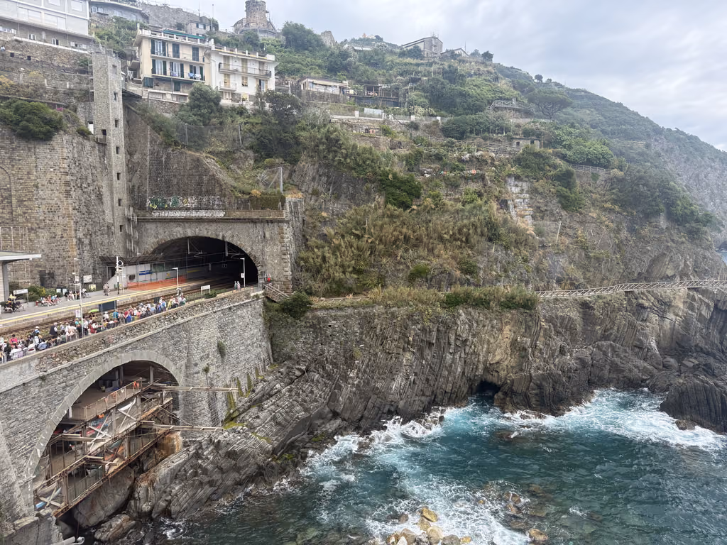 Train tunnel entrance at the Riomaggiore station in Cinque Terre with people walking along the coast.