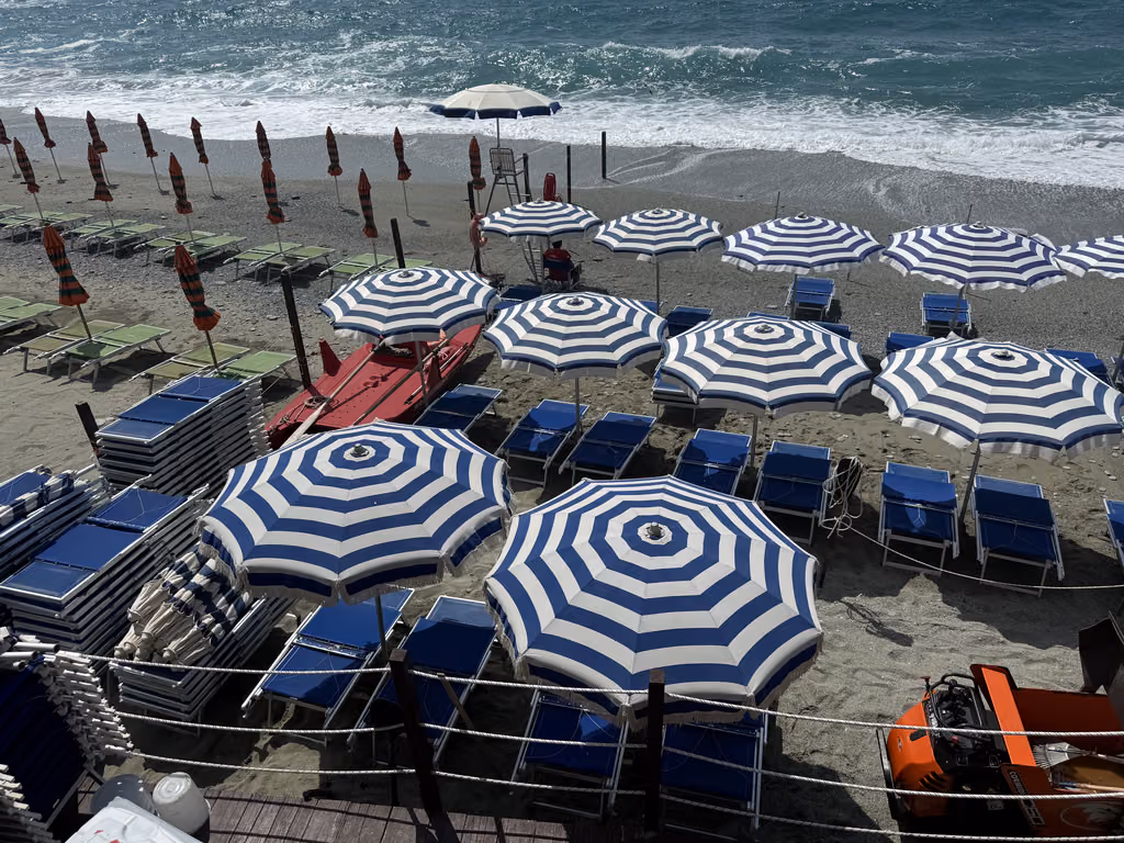 Rows of blue and white umbrellas on the sandy beach of Monterosso al Mare in Cinque Terre, Italy.