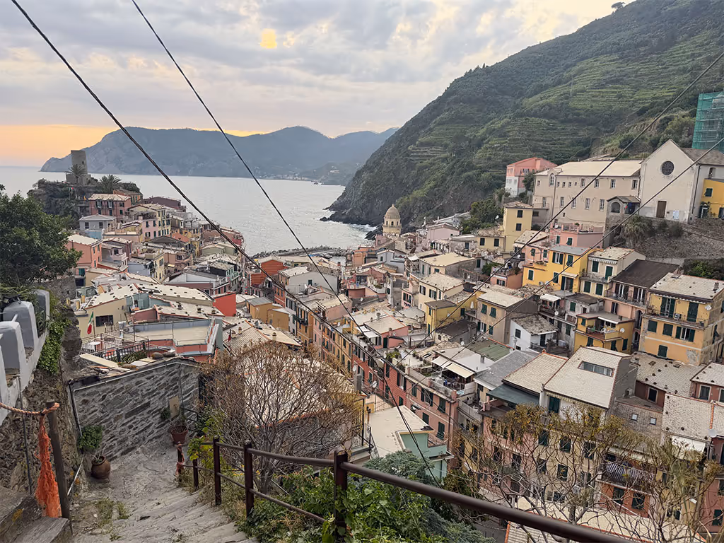 Elevated view of Vernazza harbor, colorful hillside buildings, and Ligurian coast at sunset.