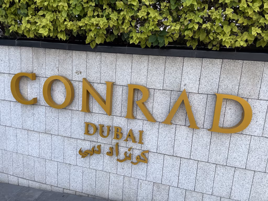 A close-up view of the golden Conrad Dubai hotel signage against a gray stone tiled wall.