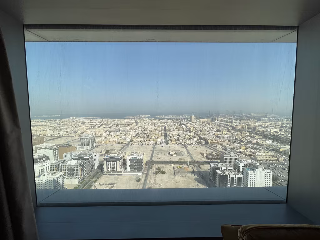 City skyline view through a large hotel room window in Dubai showing modern buildings and desert land.