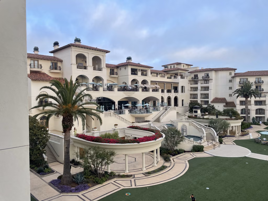 A wide outdoor view of the Laguna Cliffs Marriott Resort and Spa featuring Mediterranean architecture, arched walkways, a lush lawn, and palm trees.