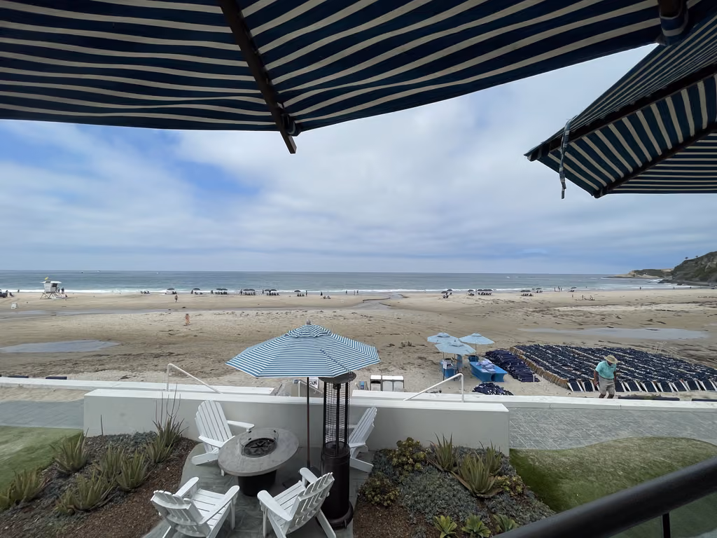 A view of the sandy beach and ocean from a patio with lounge chairs and umbrellas at the Waldorf Astoria in Dana Point.