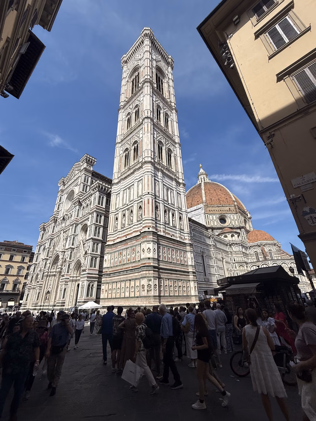 Crowded square in front of the Florence Cathedral and Giotto’s Campanile under a clear blue sky.
