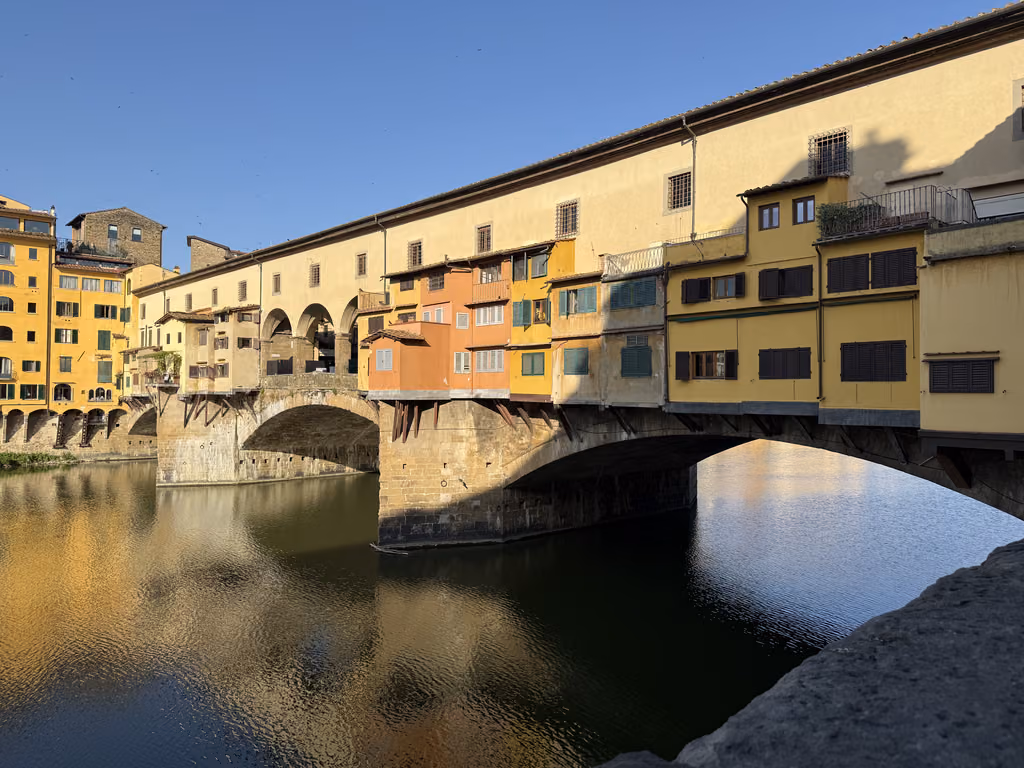 Side view of the Ponte Vecchio bridge featuring colorful buildings over the Arno River in Florence.
