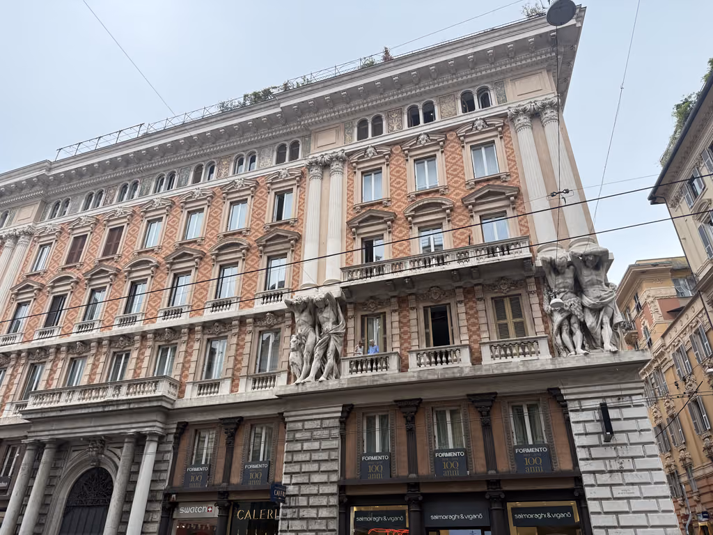 Ornate stone statues supporting a balcony on a historic building in Genoa, Italy.