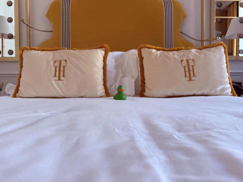 A small green rubber duck toy resting on the crisp white linens of a luxurious bed at Il Tornabuoni hotel in Florence.