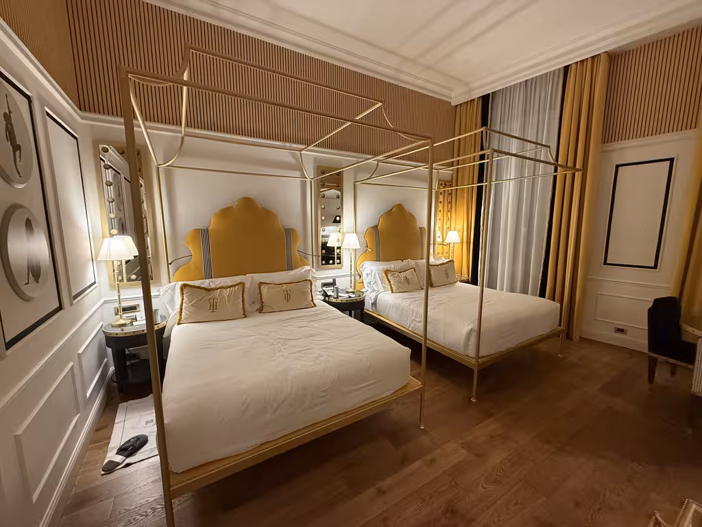 Two canopy beds with gold frames and yellow velvet headboards in a luxury hotel room at Il Tornabuoni in Florence.