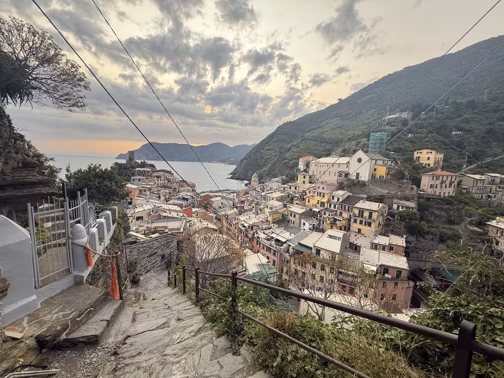 Steep stone staircase descending toward Vernazza and the Cinque Terre coastline at sunset.