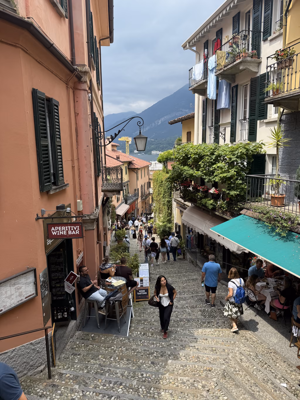 Steep, narrow cobblestone street in Varenna, Italy, lined with shops and outdoor cafes.