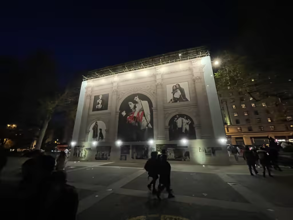 A brightly lit H&M advertising mural displayed on the exterior of a building in London at night, surrounded by people walking in the square.