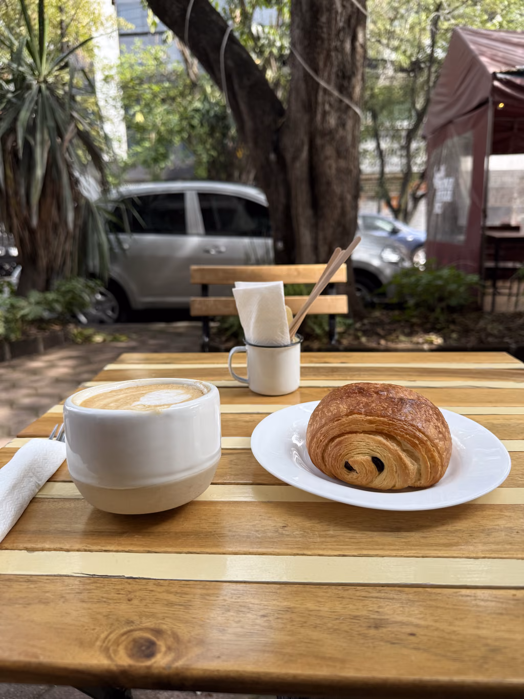 Coffee and a pain au chocolat on a wooden table at an outdoor cafe in Mexico City.