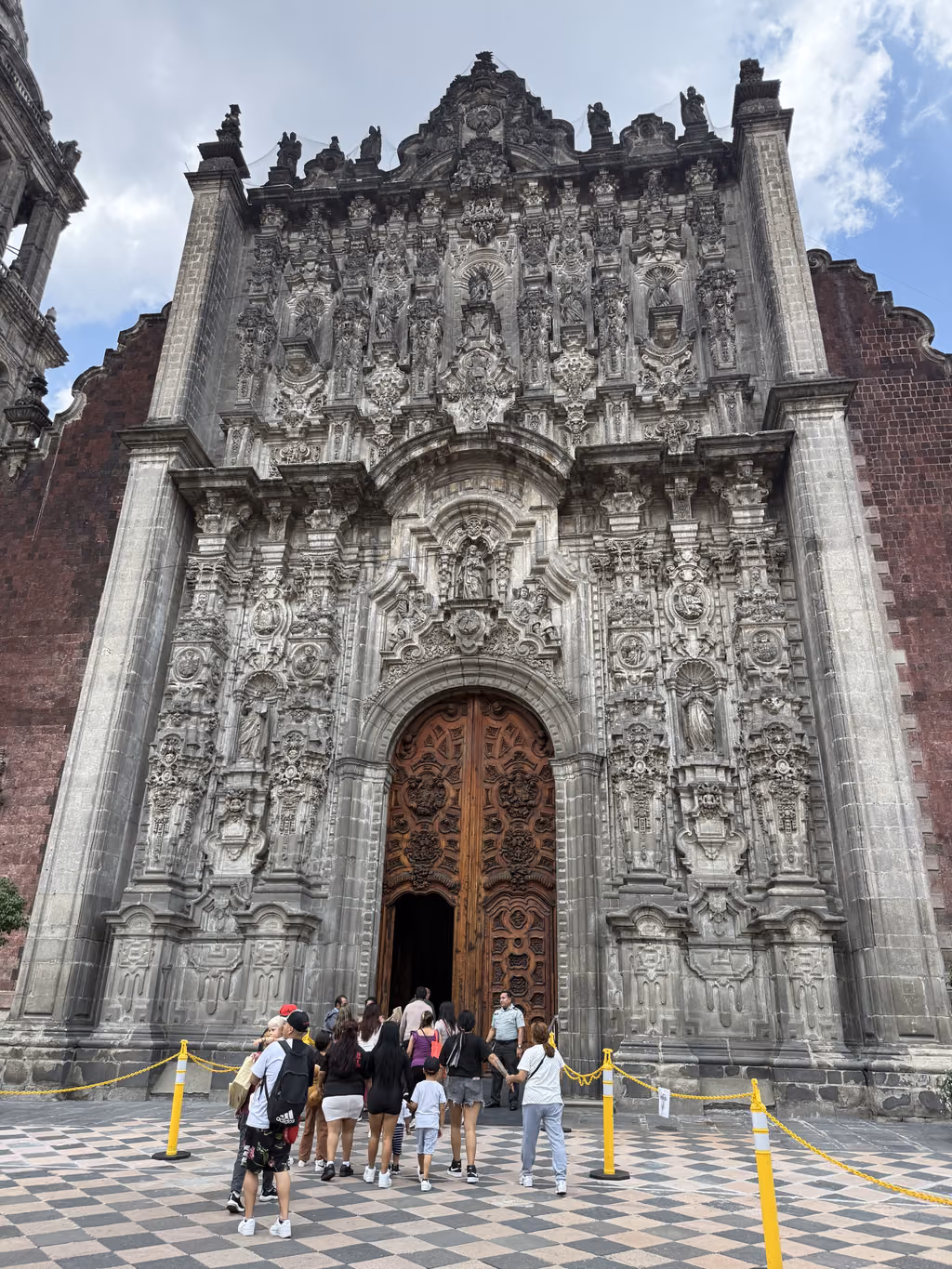 People standing before the ornate, baroque facade of the Metropolitan Cathedral in Mexico City.