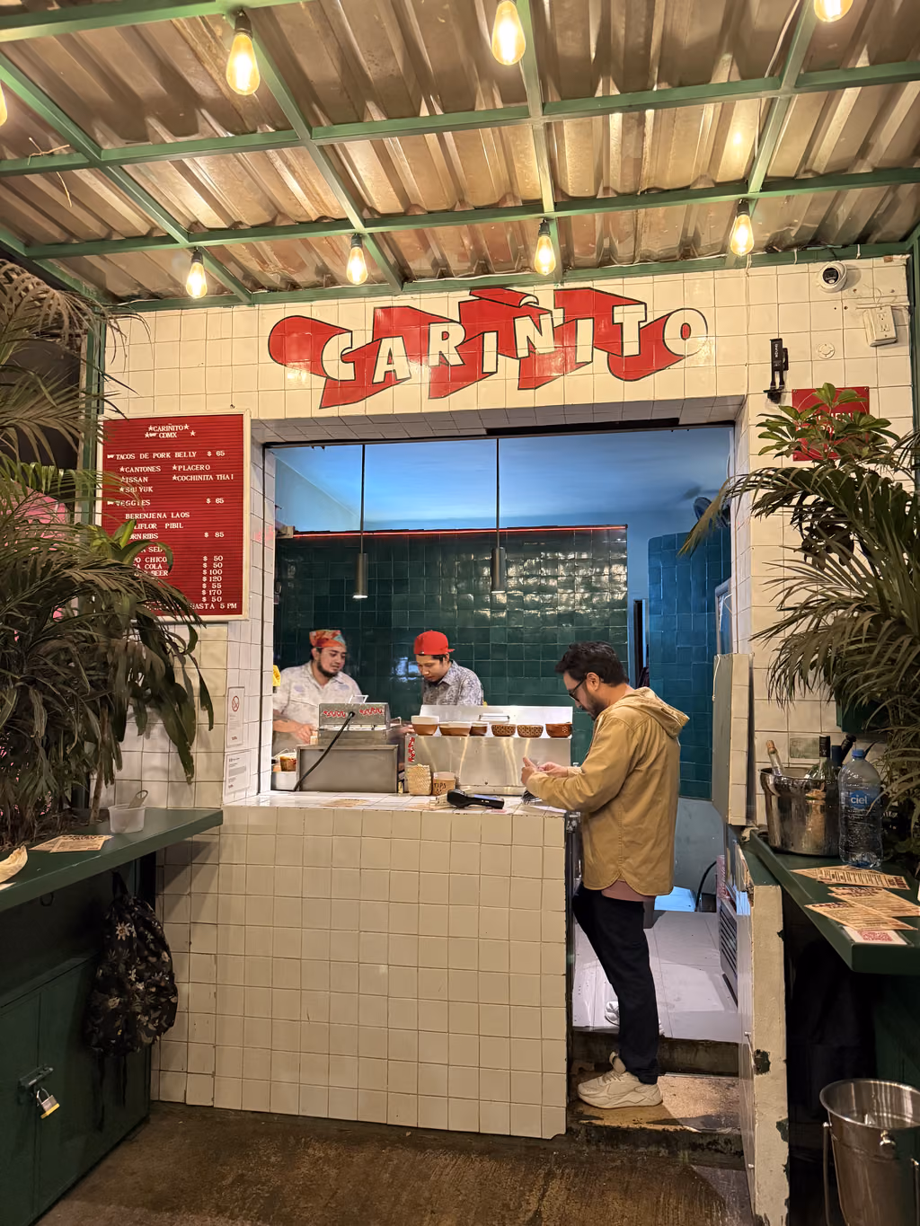 A man orders food at the Carinito taco stand in Mexico City, with staff preparing meals.