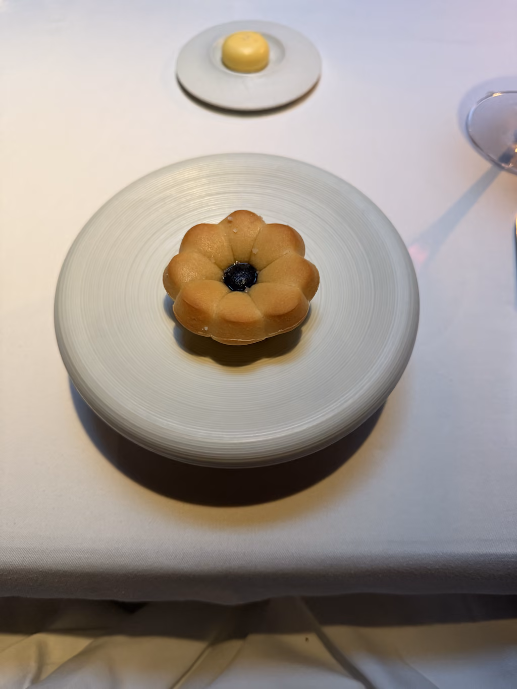 A single flower-shaped pastry with a dark jam center served on a minimalist white plate at The French Laundry.