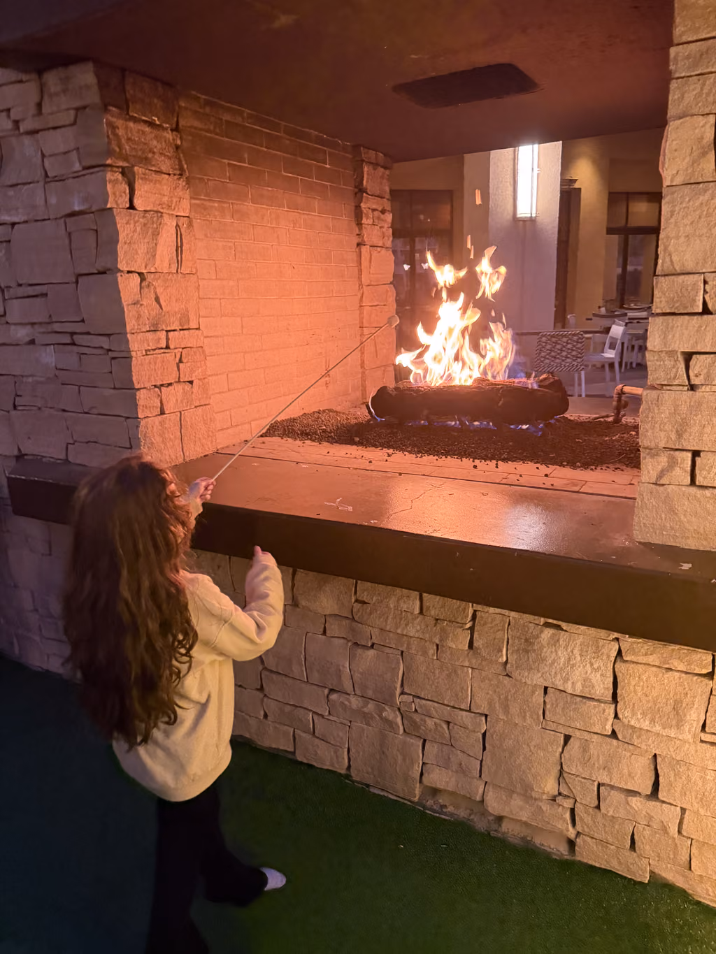 A young girl with long hair roasting a marshmallow over an outdoor fire pit at the Renaissance Palm Springs hotel.