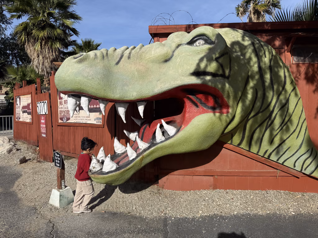 Child standing in front of a giant T-Rex head sculpture at Mr. Rex Dinosaur Adventures in Palm Springs