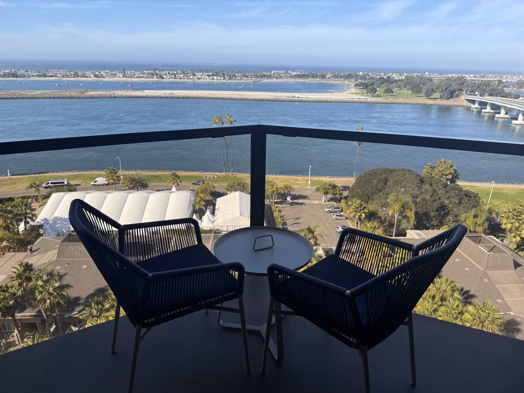 A balcony view overlooking Mission Bay in San Diego, featuring two modern outdoor chairs and a small table.