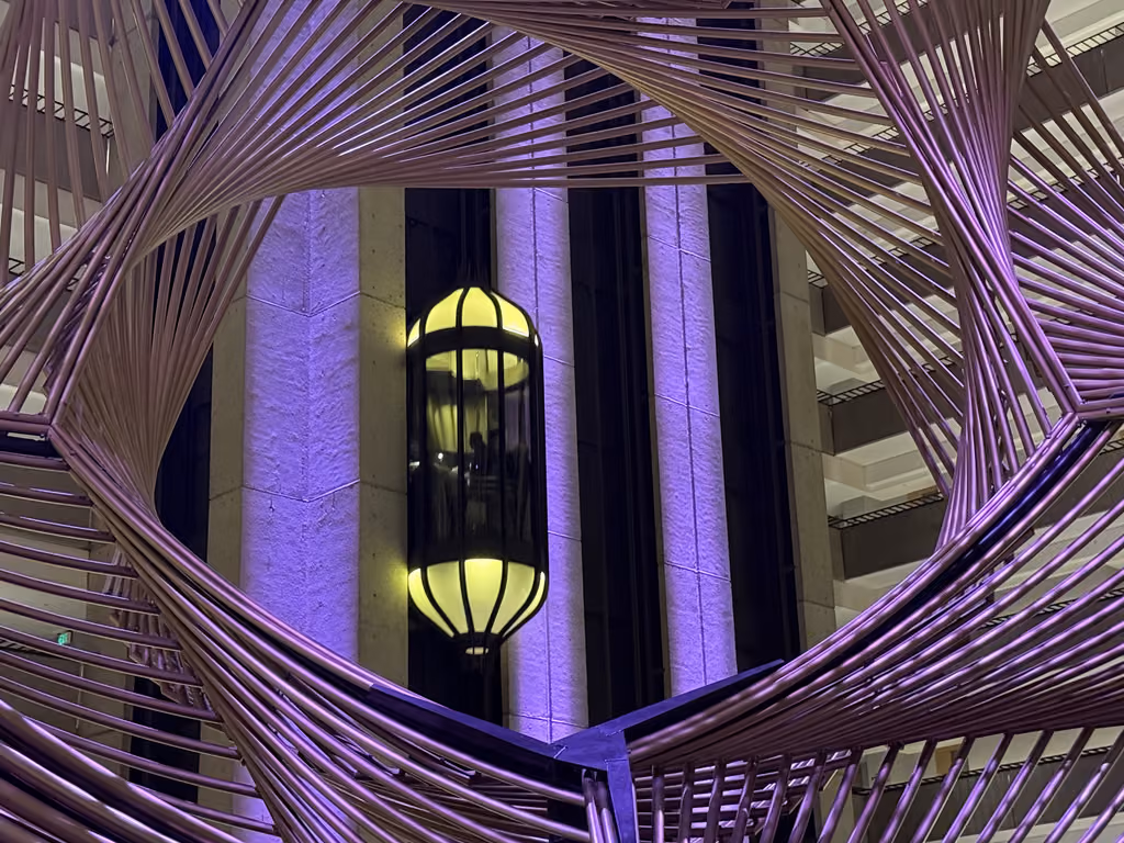 Illuminated glass elevator inside the Hyatt Regency San Francisco atrium with metal sculpture.