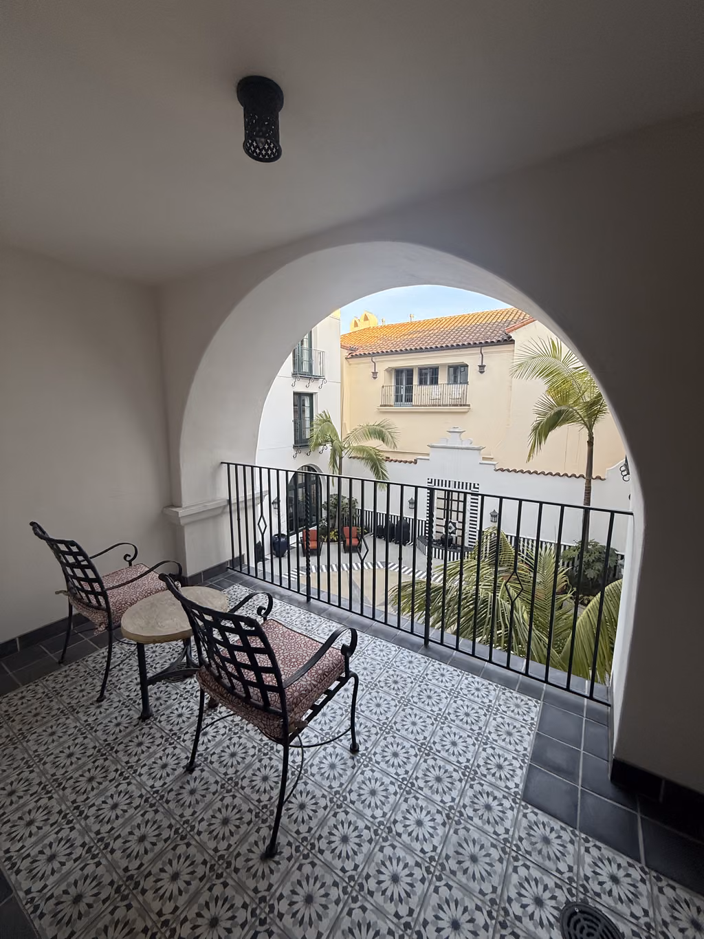 A balcony view with patterned tile flooring and two chairs overlooking a lush Mediterranean-style courtyard at the Hotel Californian in Santa Barbara.
