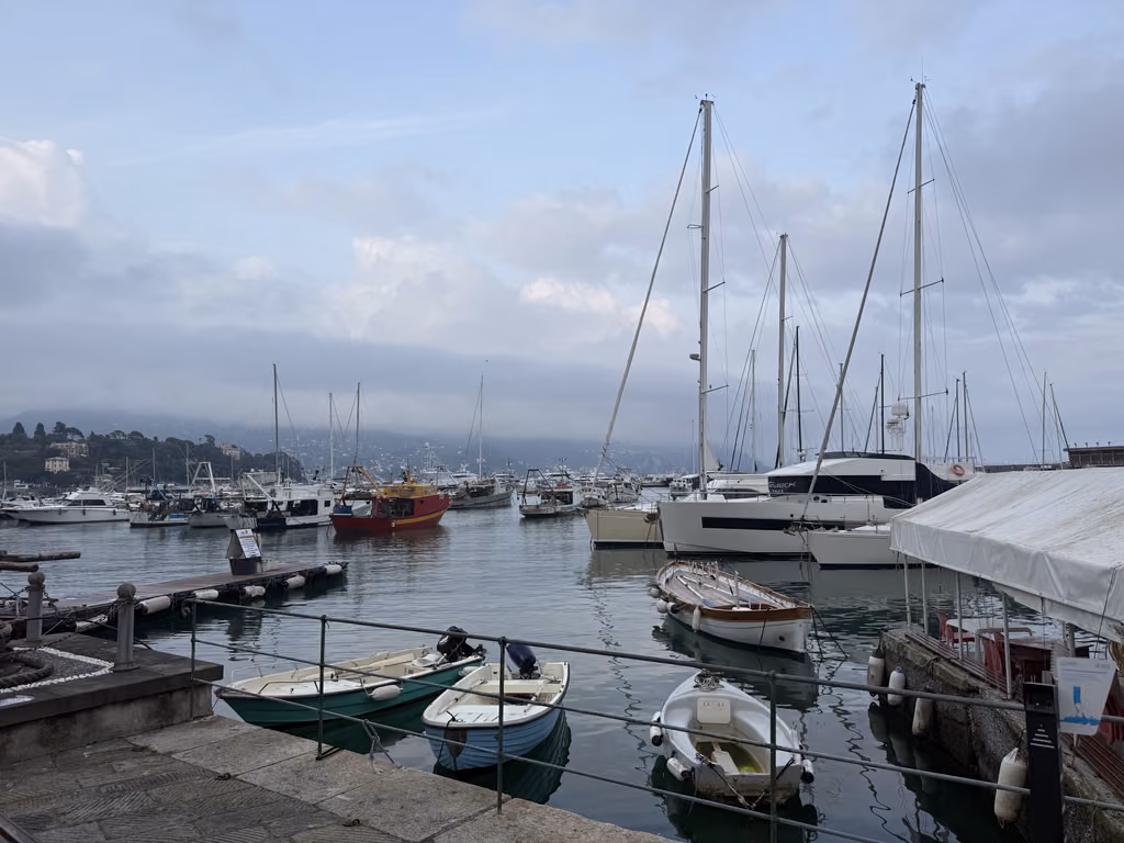Boats and yachts docked in the tranquil harbor of Santa Margherita Ligure under a cloudy sky.