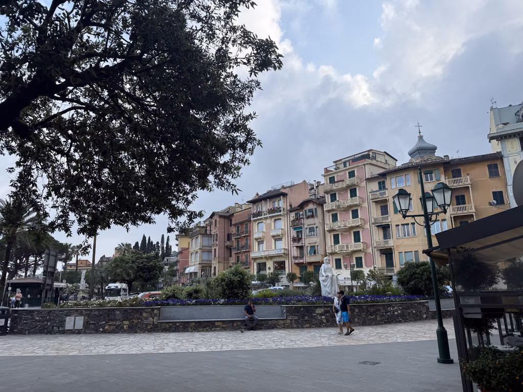 People walking by a white statue in a sunlit town square in Santa Margherita Ligure, Italy.
