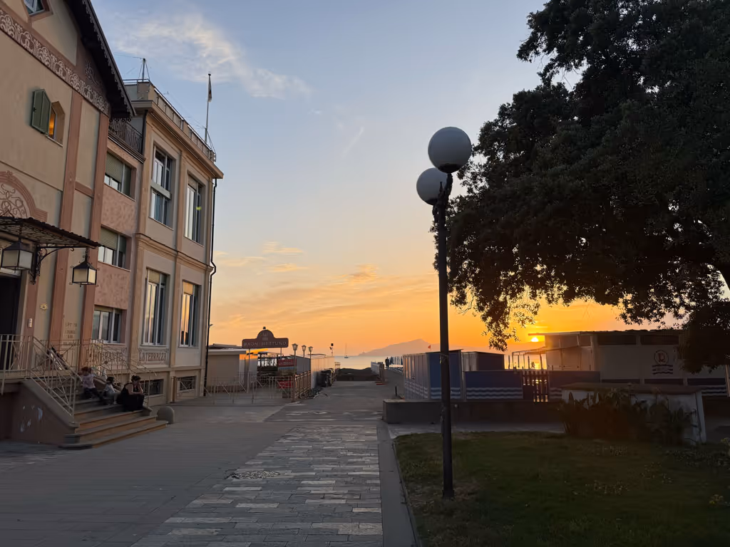 Sunset over the Sestri Levante boardwalk with historic buildings and trees along the coastline.