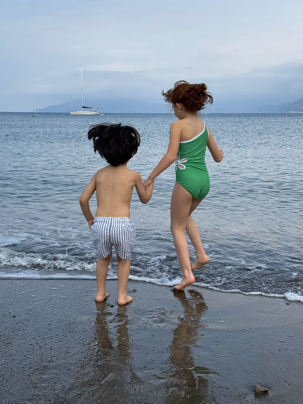Two children holding hands while jumping into the water at Baia delle Favole in Sestri Levante.