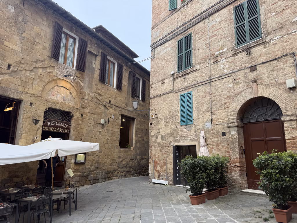 Narrow, cobblestone street in Siena, Italy, featuring historic stone buildings and a restaurant.