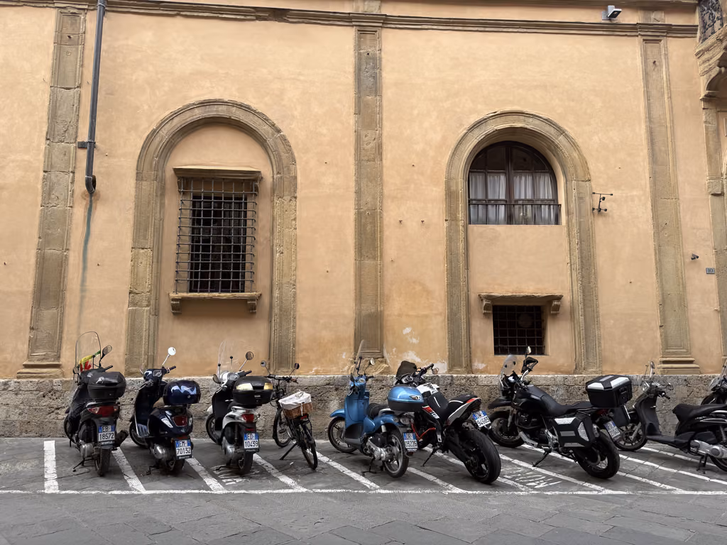 Motorcycles and scooters parked along a historic wall in Siena, Italy.
