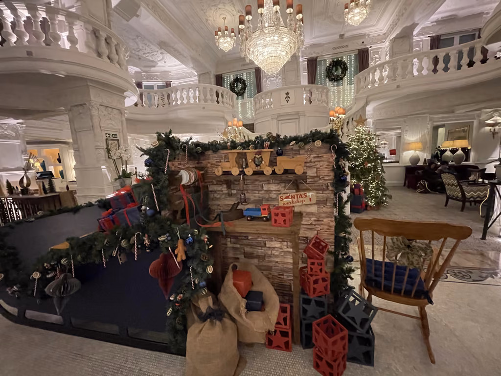 The decorated hotel lobby at St. Ermin's Hotel in London features a miniature Santa's workshop display with holiday lights, a large chandelier, and a rocking chair.