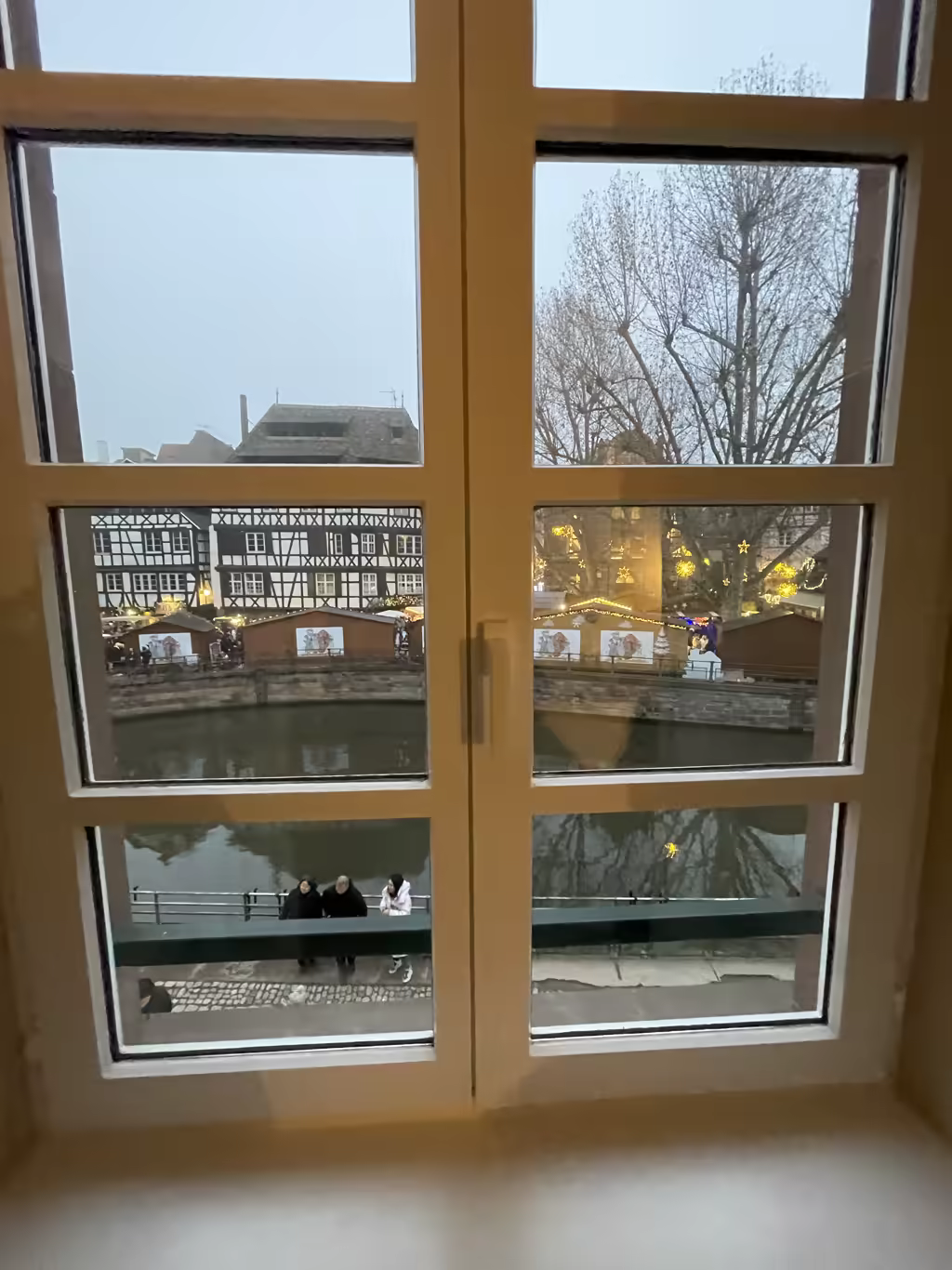 View of Petit France Christmas market stalls and canal in Strasbourg through a window.