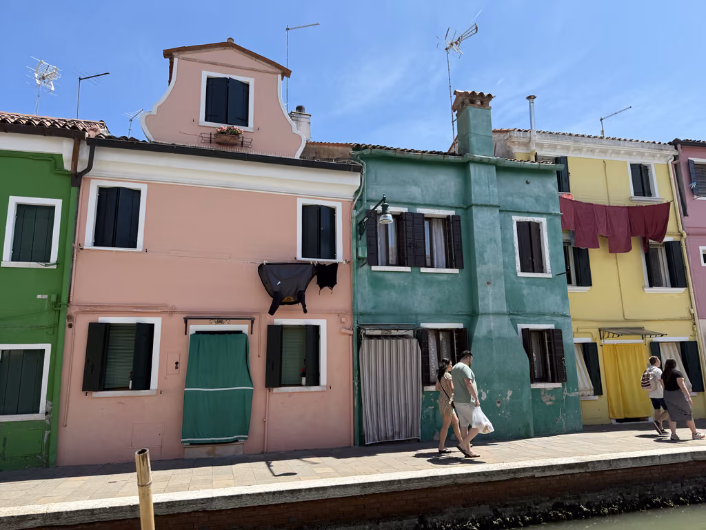 Vibrant colorful houses along a canal in Burano, Italy, with people walking on the sidewalk.