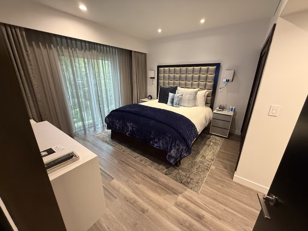 A luxurious bedroom with a king-sized bed, tufted headboard, and sliding glass doors leading to a balcony at the Sunset Marquis hotel in West Hollywood.